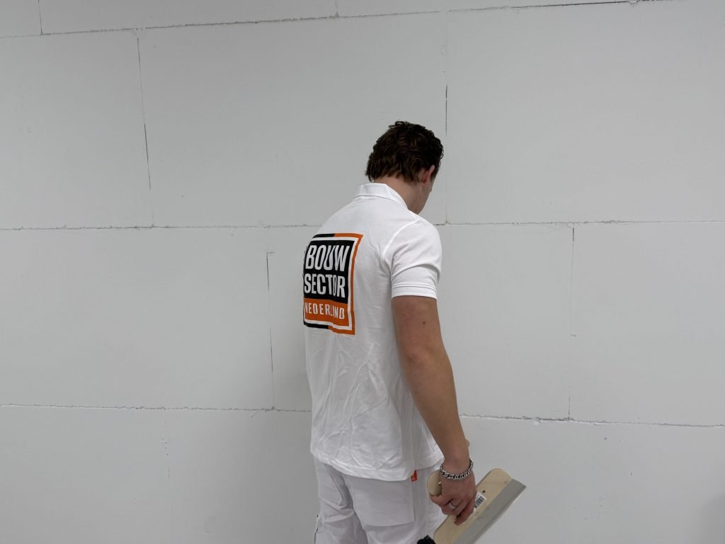 Stukadoor met een plamuurmes in de hand bekijkt een wand van gipsblokken van dichtbij